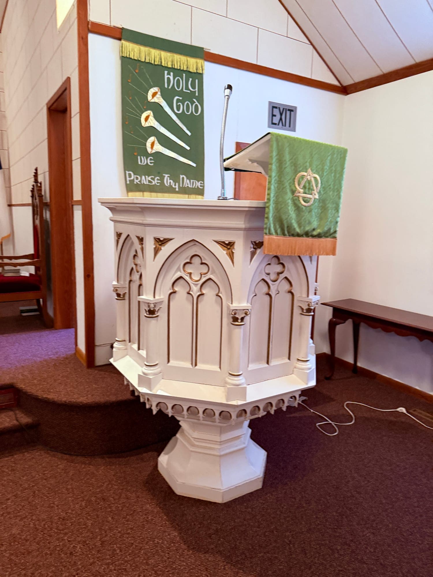 The white Gothic pulpit of Calvary Lutheran Church beneath a banner reading Holy God, We Praise Thy Name
